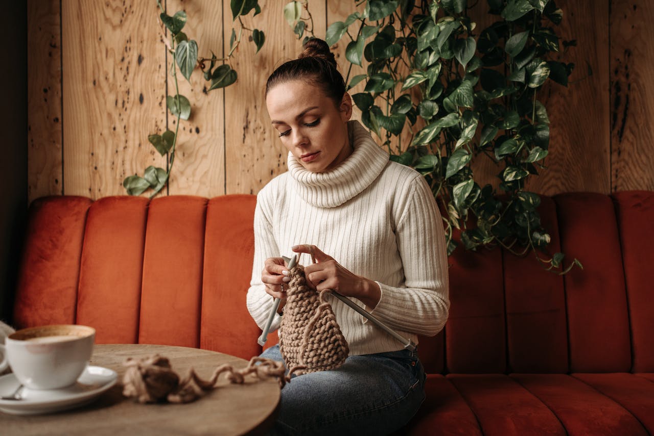Woman in Sweater Sitting on a Couch Knitting