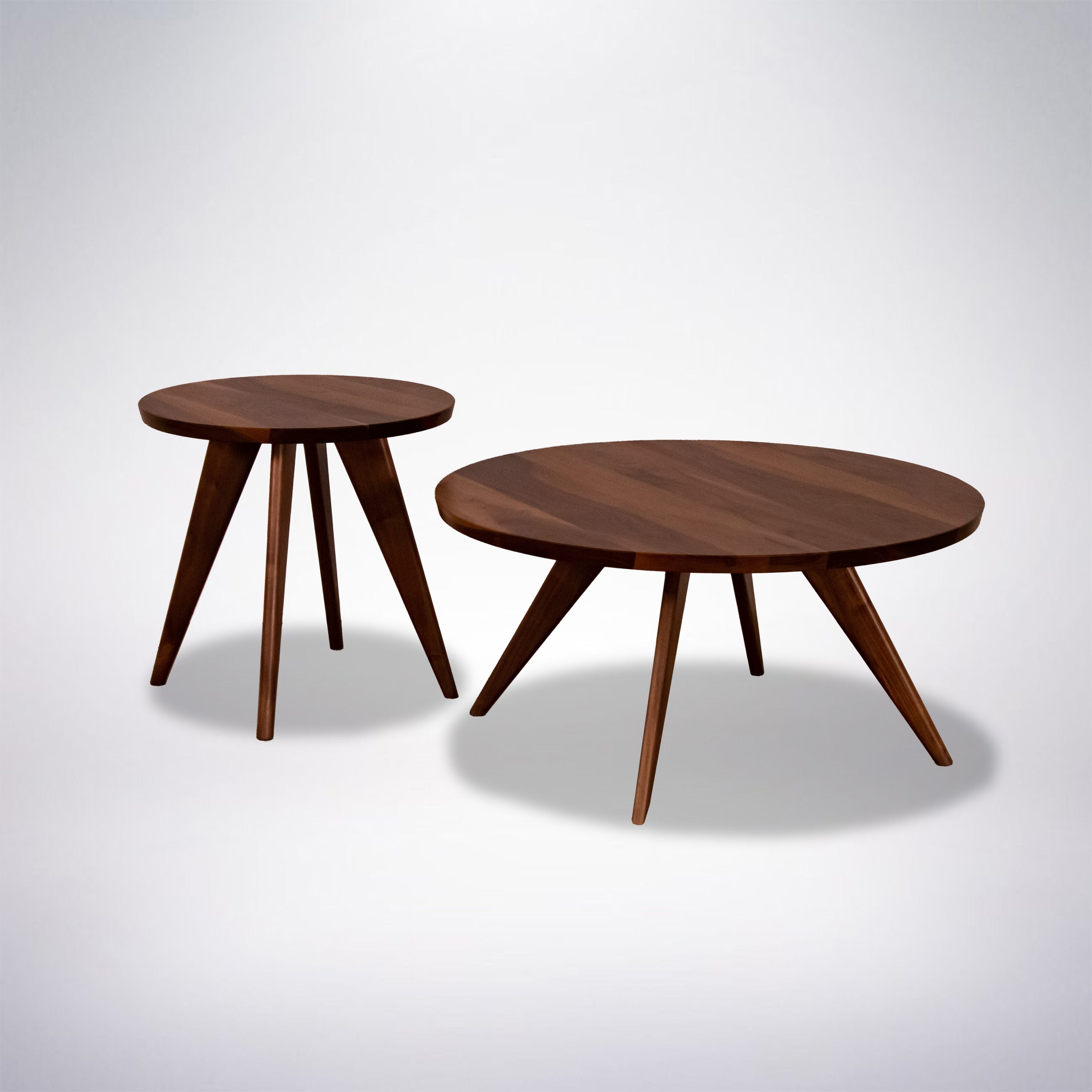 Two wooden tables with round tops and angled legs, one larger and one smaller, both in a mid-century modern style, set against a plain light background.