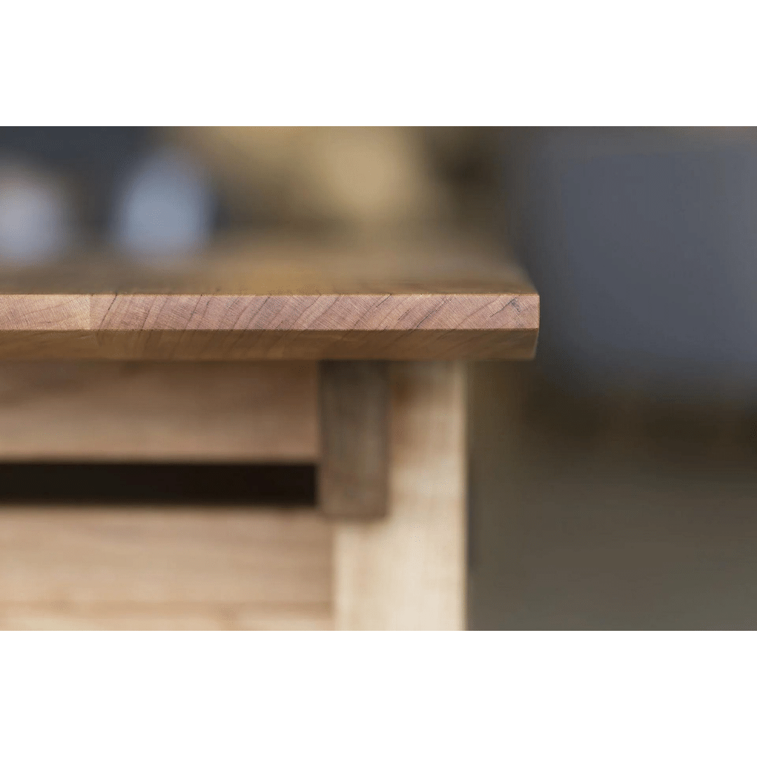 Close-up of the Enso Side Table With Drawer by TY Fine Furniture, crafted from solid wood. The smooth, handcrafted edge highlights the natural grain, while a blurred background emphasizes the artistry of this organic, handmade piece.