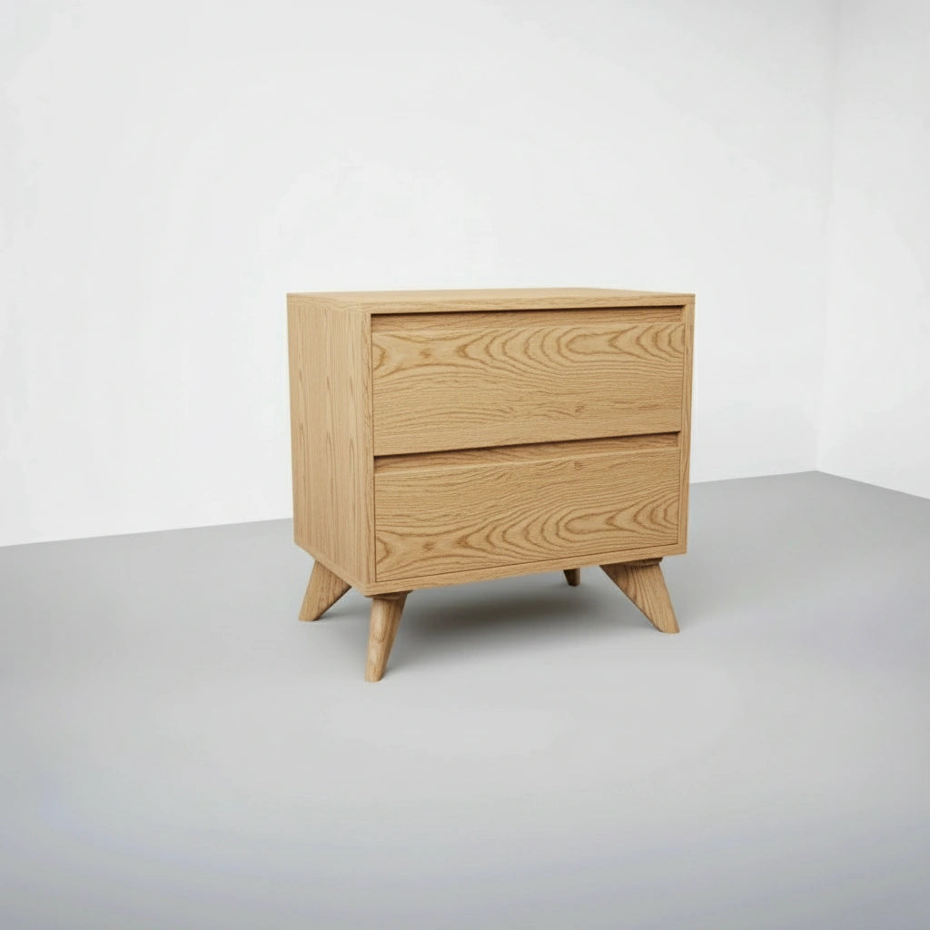 The Modern Cube Side Table by TY Fine Furniture, crafted from solid white oak, stands on angled legs against a white wall in a minimalist room, featuring two drawers with Italian push-to-open slides for easy access.