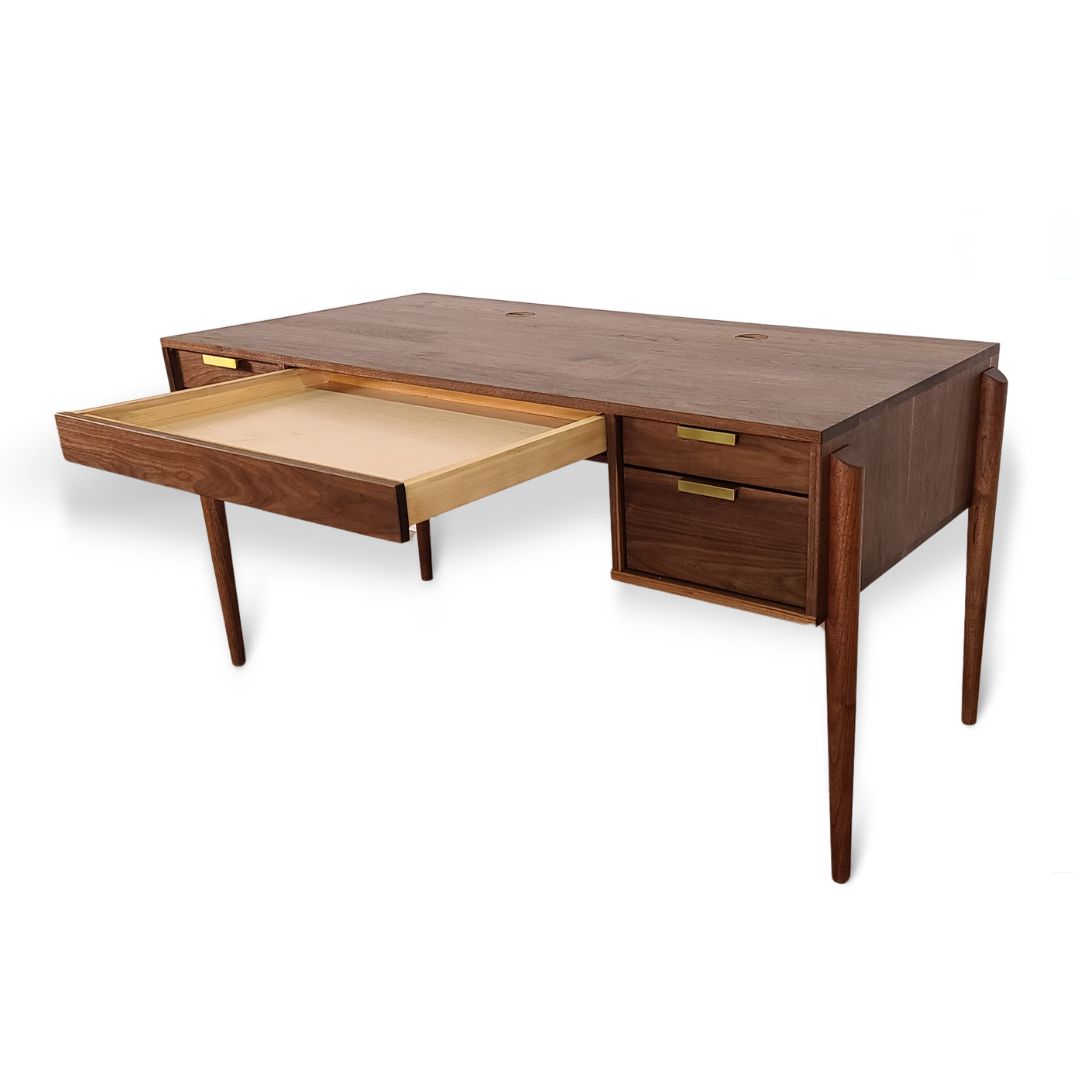 The Apollo Solid Wood Executive Desk by TY Fine Furniture features four tapered legs, three right-side drawers, a large open center drawer, brass handles, and a smooth finish—handcrafted in Columbus, Ohio for a stylish home office.