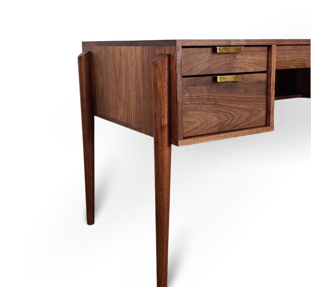 A close-up of the TY Fine Furniture Apollo Solid Wood Executive Desk—handcrafted in Columbus, Ohio—with tapered legs, two brass-handled drawers, and rich wood grain, shown against a white background for a stylish home office.