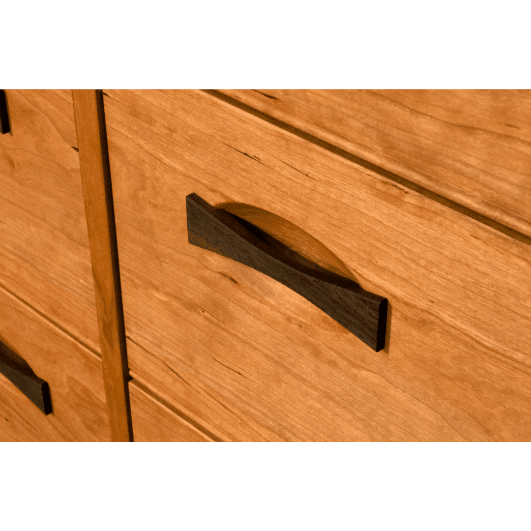 Close-up of the Enso 6/8 Drawer Dresser by TY Fine Furniture, featuring handcrafted cherry wood and a curved dark handle casting a unique shadow across the light drawer front.