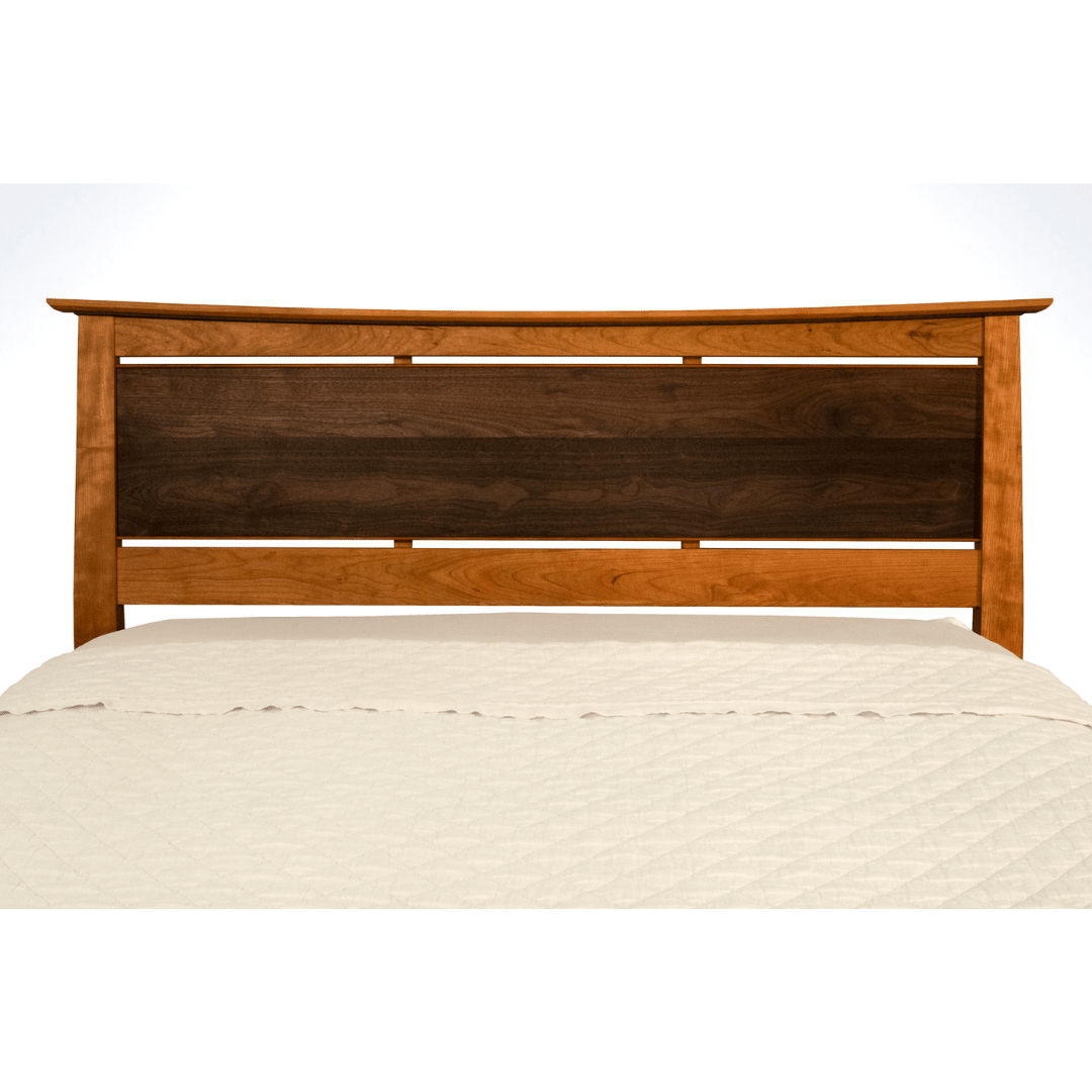 The Enso Platform Bed Cherry by TY Fine Furniture features a curved headboard with a dark central panel and lighter wood frame, topped with a cream-colored textured quilt.