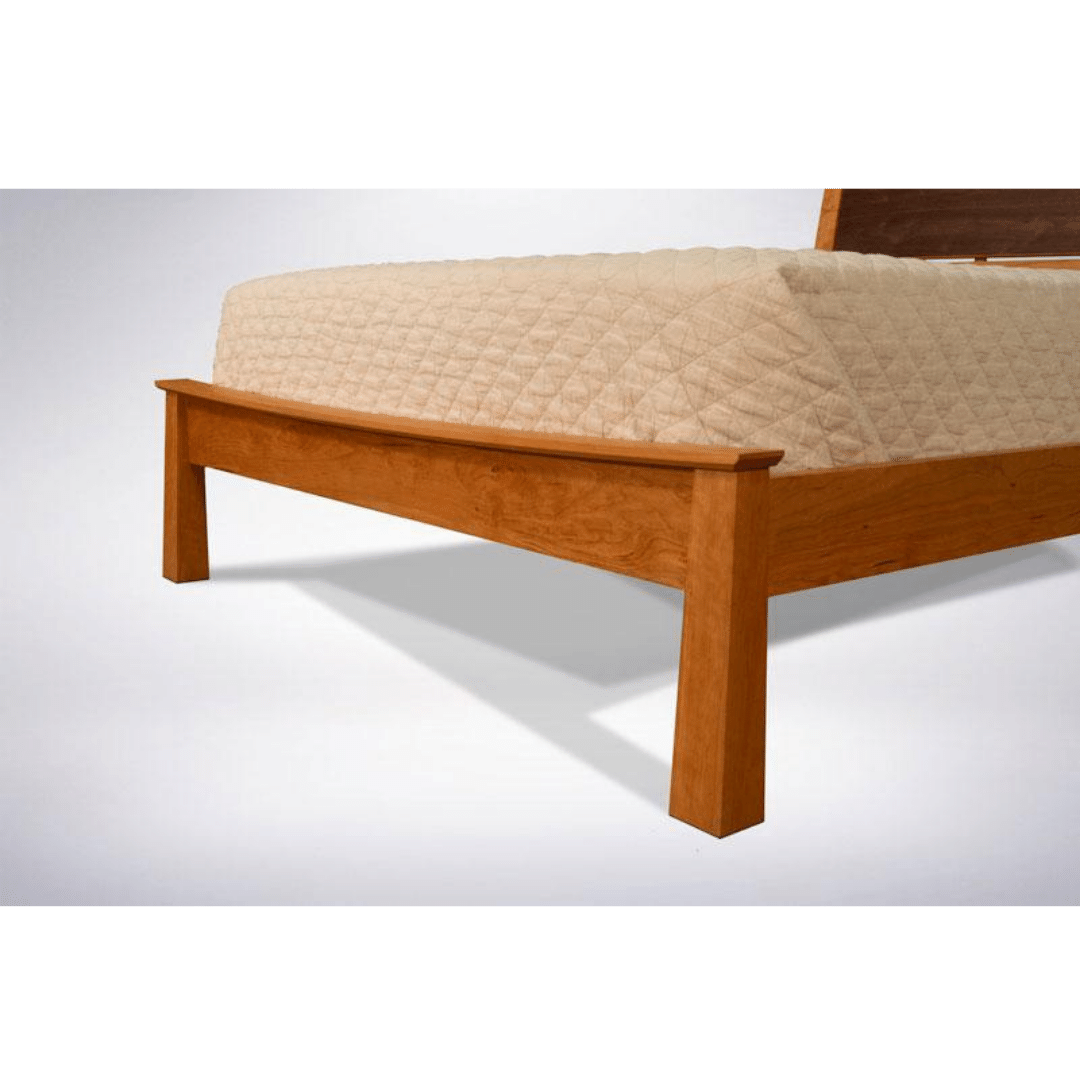 The Enso Platform Bed Cherry by TY Fine Furniture features a solid wood frame with a light brown finish, shown from the foot of the bed and topped with a neatly made, cream-colored quilted coverlet.