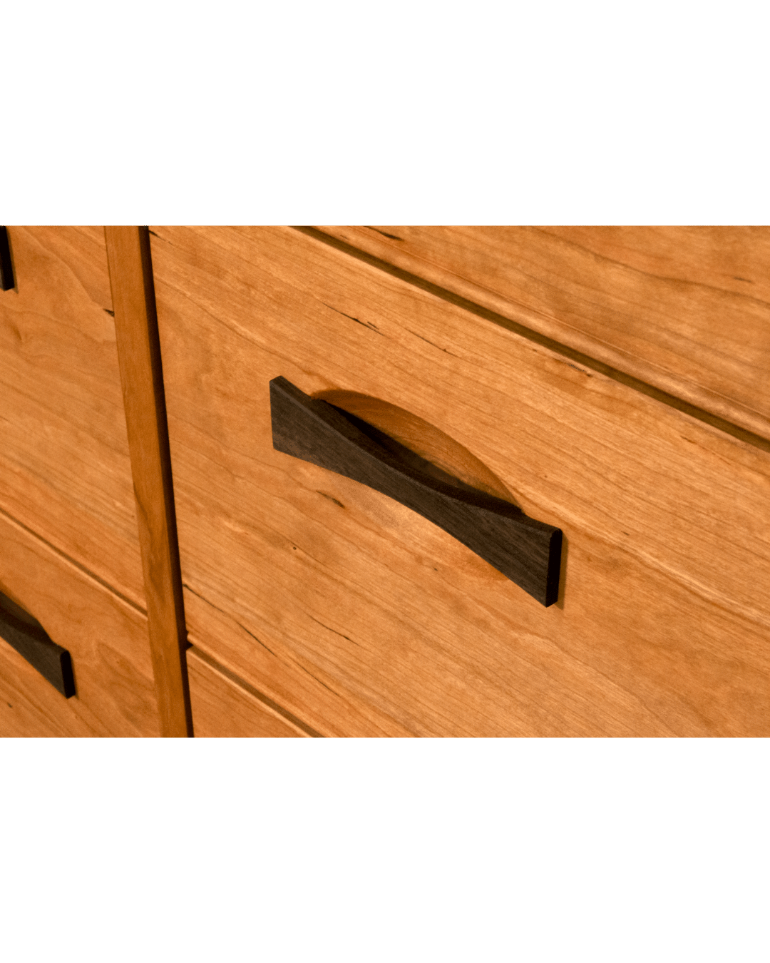 Close-up of the TY Fine Furniture Enso 5-Drawer Upright Dresser in cherry. Handmade from solid wood, it features a warm finish, visible grain, and elegant dark curved handles on each drawer.