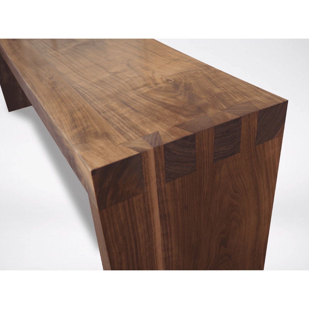 A close-up of the Enso Solid Wood Bench by TY Fine Furniture shows dovetail joinery at the corner. Handcrafted in Columbus, Ohio from polished dark walnut with visible grain, it highlights Japanese woodworking against a plain white background.