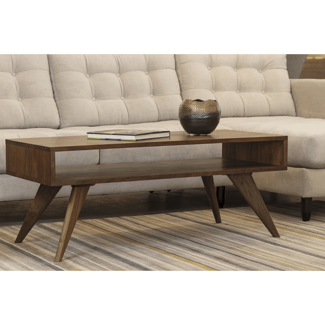 The TY Fine Furniture Modern Coffee Table in Walnut - Solid Wood adds mid-century modern style to a beige tufted sofa, featuring angled legs and displayed on a striped rug with a book and decorative bowl. Available in Columbus, OH.