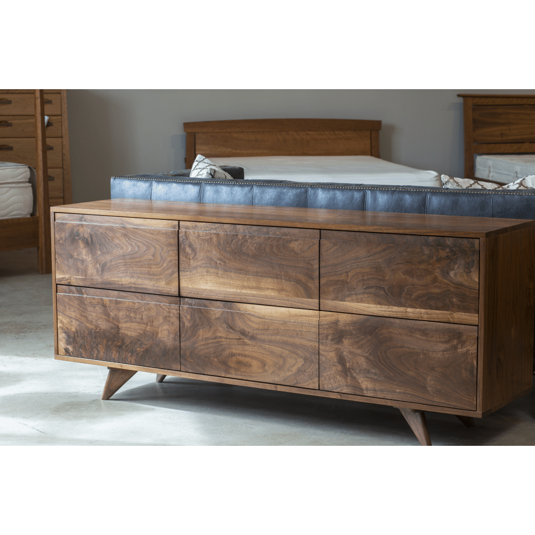 The TY Fine Furniture Modern Dresser, a mid-century solid cherry piece with six drawers and angled legs, sits on a light floor beside a bed and other wooden furniture, showcasing its timeless design.