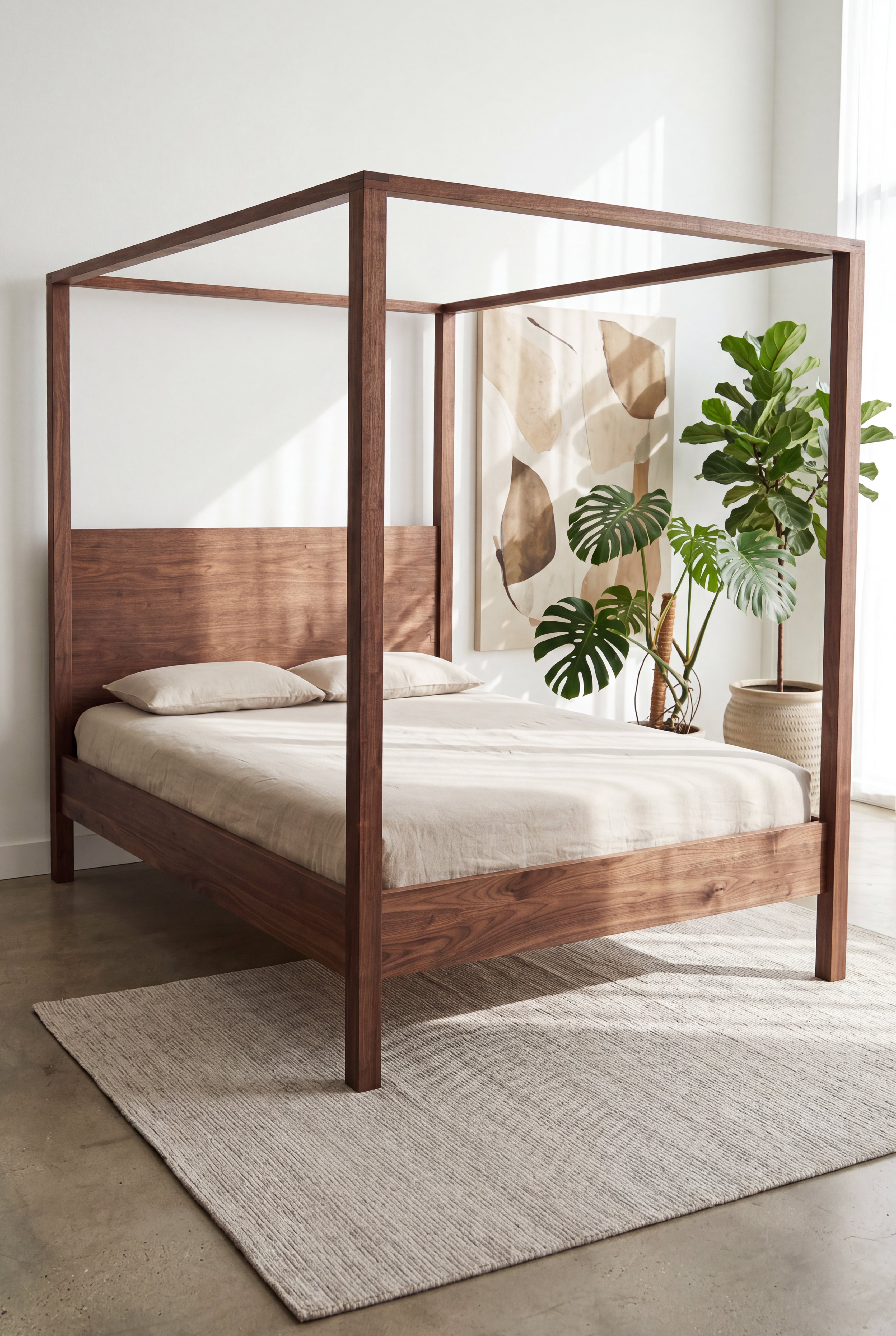 A Modern Four Poster Bed - Solid Wood-Walnut by TY Fine Furniture with beige bedding sits atop a textured rug. A large potted plant and abstract wall art decorate the bright, minimalist bedroom, illuminated by sunlight streaming in.