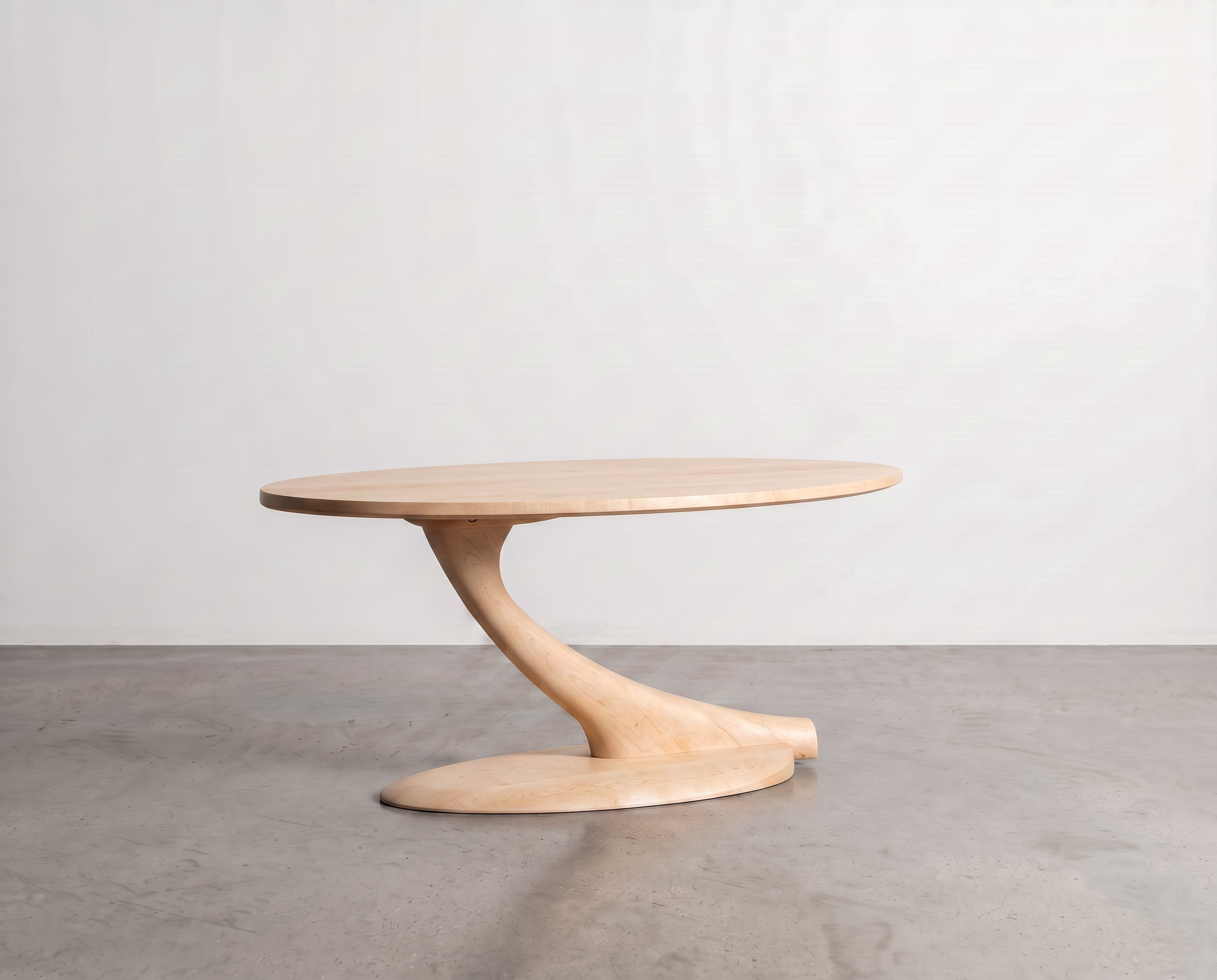 A minimalist Cantilever Oval Coffee Table Solid Wood - Maple by TY Fine Furniture, featuring a sculptural, curved pedestal base and a light maple finish, is centered against a plain white wall on a gray concrete floor.