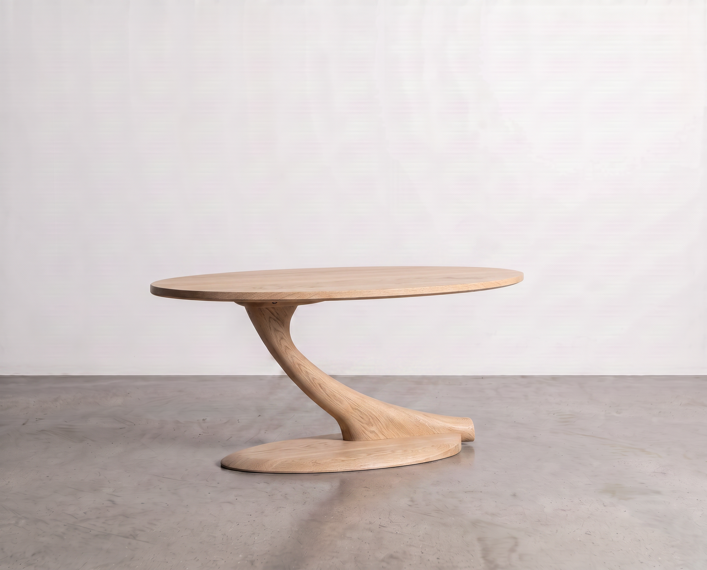 A modern Cantilever Oval Coffee Table Solid Wood - Maple by TY Fine Furniture, featuring a twisted sculptural base, sits on a polished concrete floor against a plain white wall, showcasing the impeccable craftsmanship of this handcrafted maple piece.