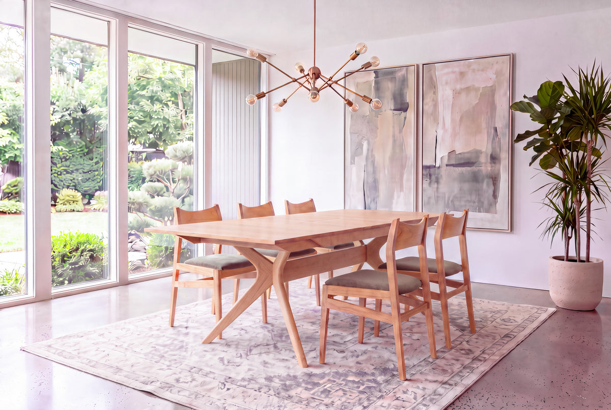 Modern dining room featuring the Solid Maple Extendable Dining Table from the Strata Collection by TY Fine Furniture, paired with six chairs, abstract wall art, a large potted plant, and floor-to-ceiling windows overlooking a lush green garden.