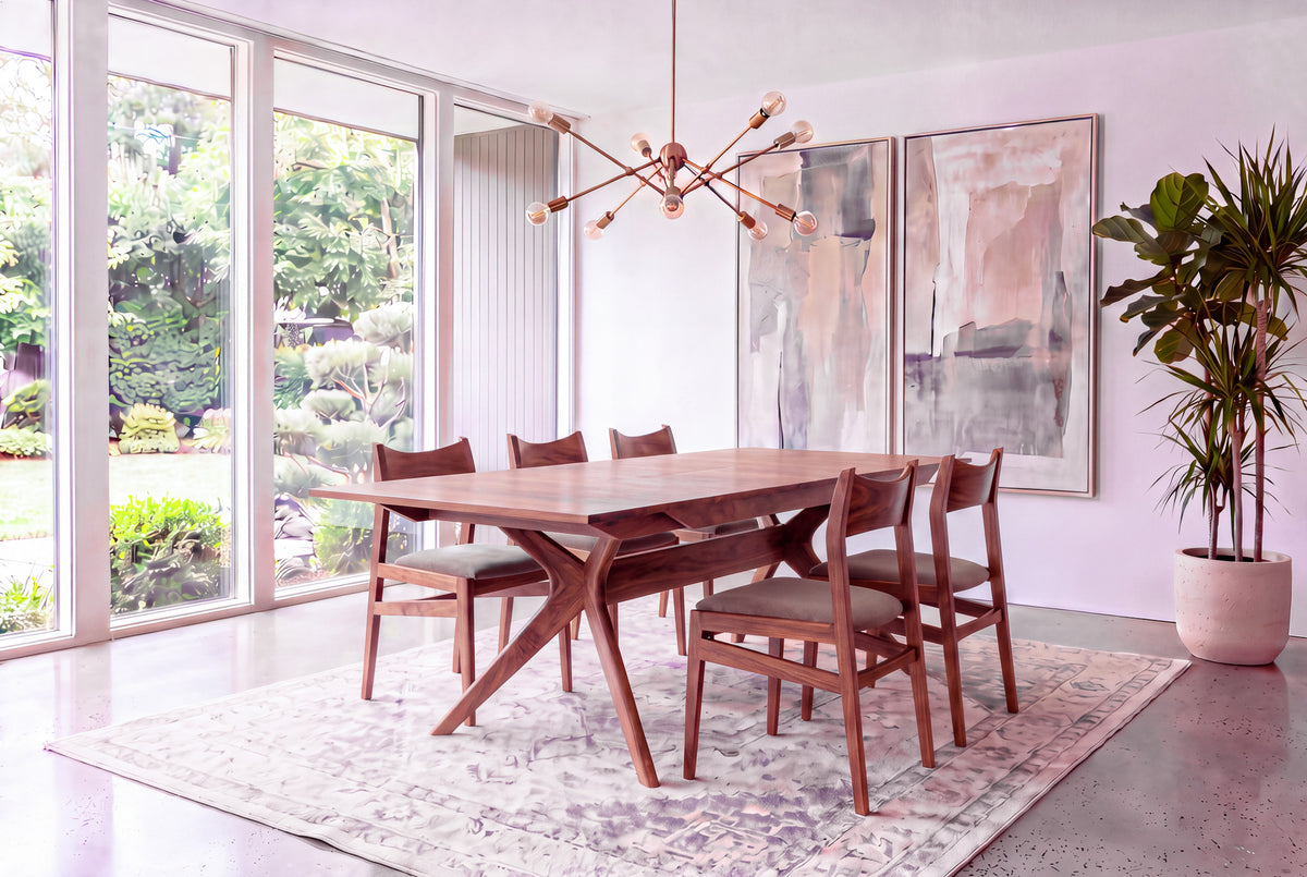 Certainly! Here’s your rewritten sentence, integrating the product data: A modern dining room featuring the Solid Walnut Extendable Dining Table from the Strata Collection by TY Fine Furniture, paired with six chairs atop a patterned rug; large windows reveal a garden view, complemented by abstract wall art, a potted plant, and a contemporary light fixture overhead.