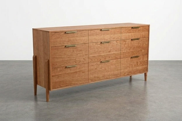 The Solid Cherry 9-Drawer Triple Bank Dresser from the Apollo Collection by TY Fine Furniture features handcrafted solid cherry wood construction, nine spacious drawers with sleek brass handles, and stands on a gray concrete floor against a plain white wall—bringing timeless mid-century style to any interior.