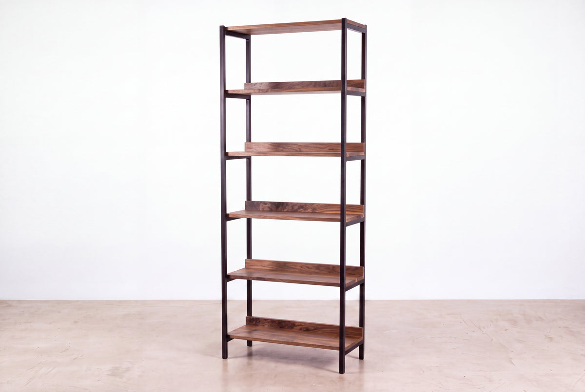 The Solid Walnut Tall Mid-Century Bookcase - Essentials Collection | TY Fine Furniture features a black metal frame and solid wood shelves, standing on a light floor against a plain white wall.