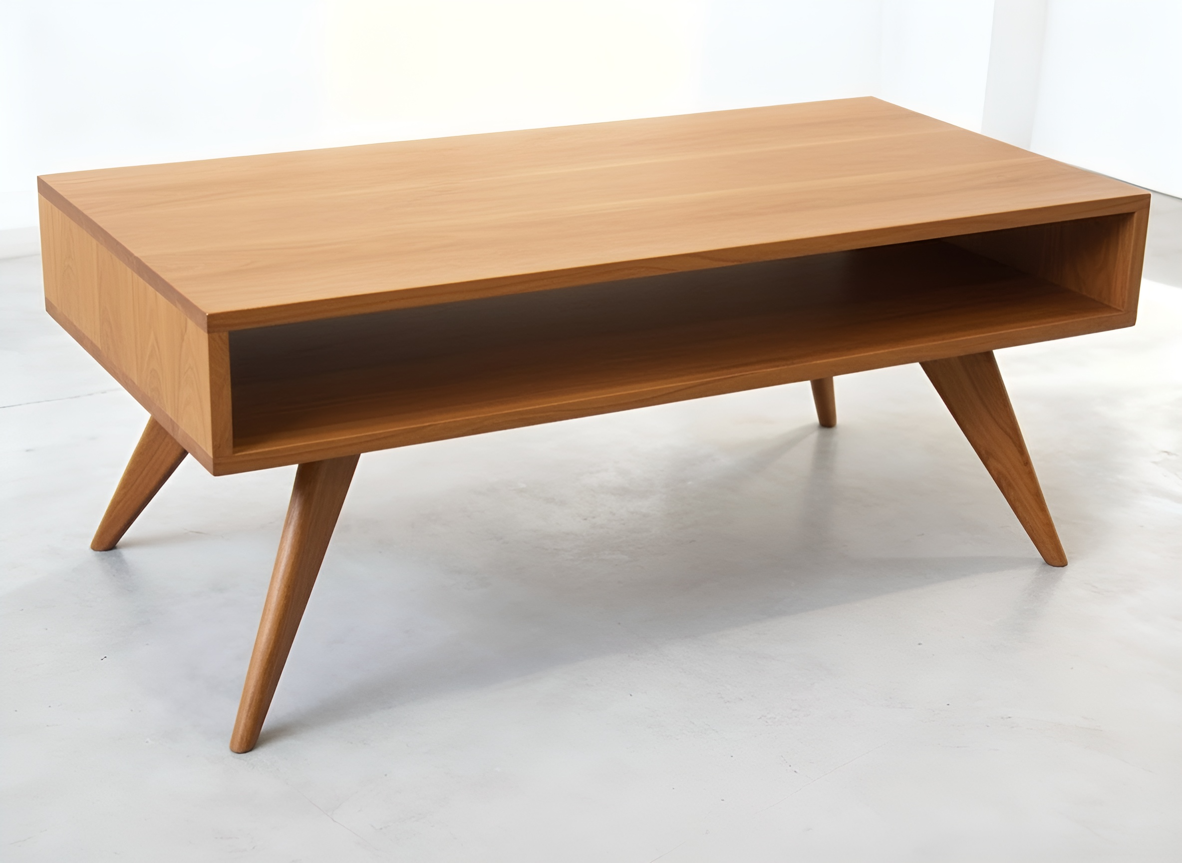 The TY Fine Furniture Modern Coffee Table features solid cherry wood, angled legs, and an open shelf. Handmade in a mid-century modern style, it’s shown in a bright minimalist space.