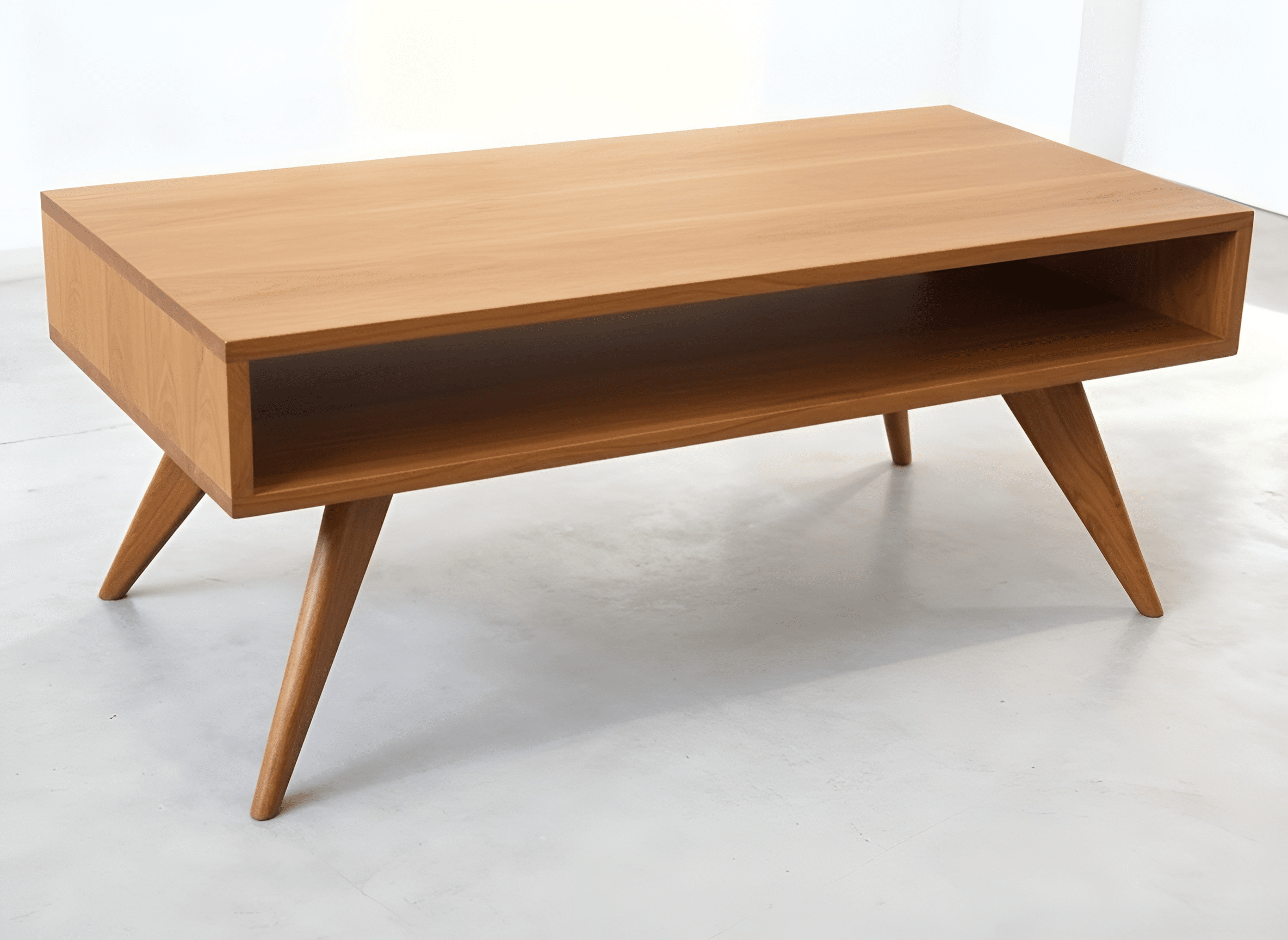 The Modern Coffee Table - Solid Wood by TY Fine Furniture features angled legs and an open lower shelf, crafted from cherry wood, shown in a bright, minimal room with a light floor.
