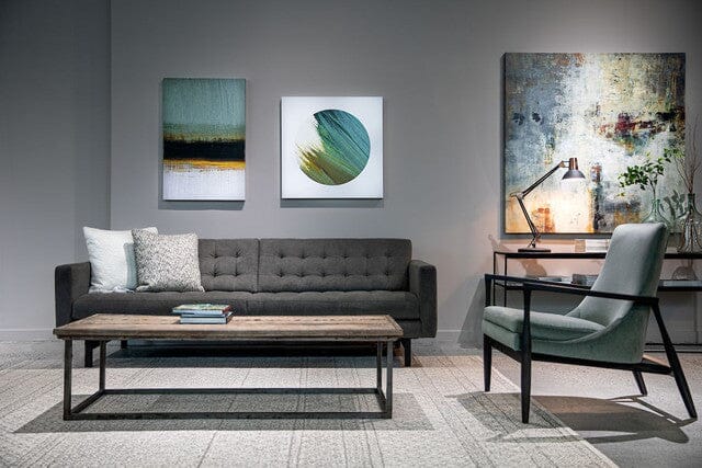 Modern living room with an American Leather PARKER Mid Sofa and Chair, wooden coffee table, light gray armchair, abstract art, desk with lamp, and minimalist decor on a patterned rug. Neutral tones and soft lighting enhance the cozy atmosphere.