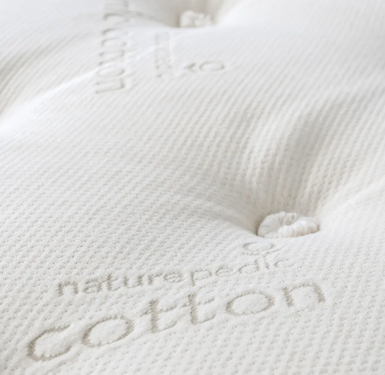 Close-up of the Naturepedic Concerto Plush Pillow Top Mattress, showing its textured white organic surface with "naturepedic cotton" stitched into the fabric and detailed tufted button accents.