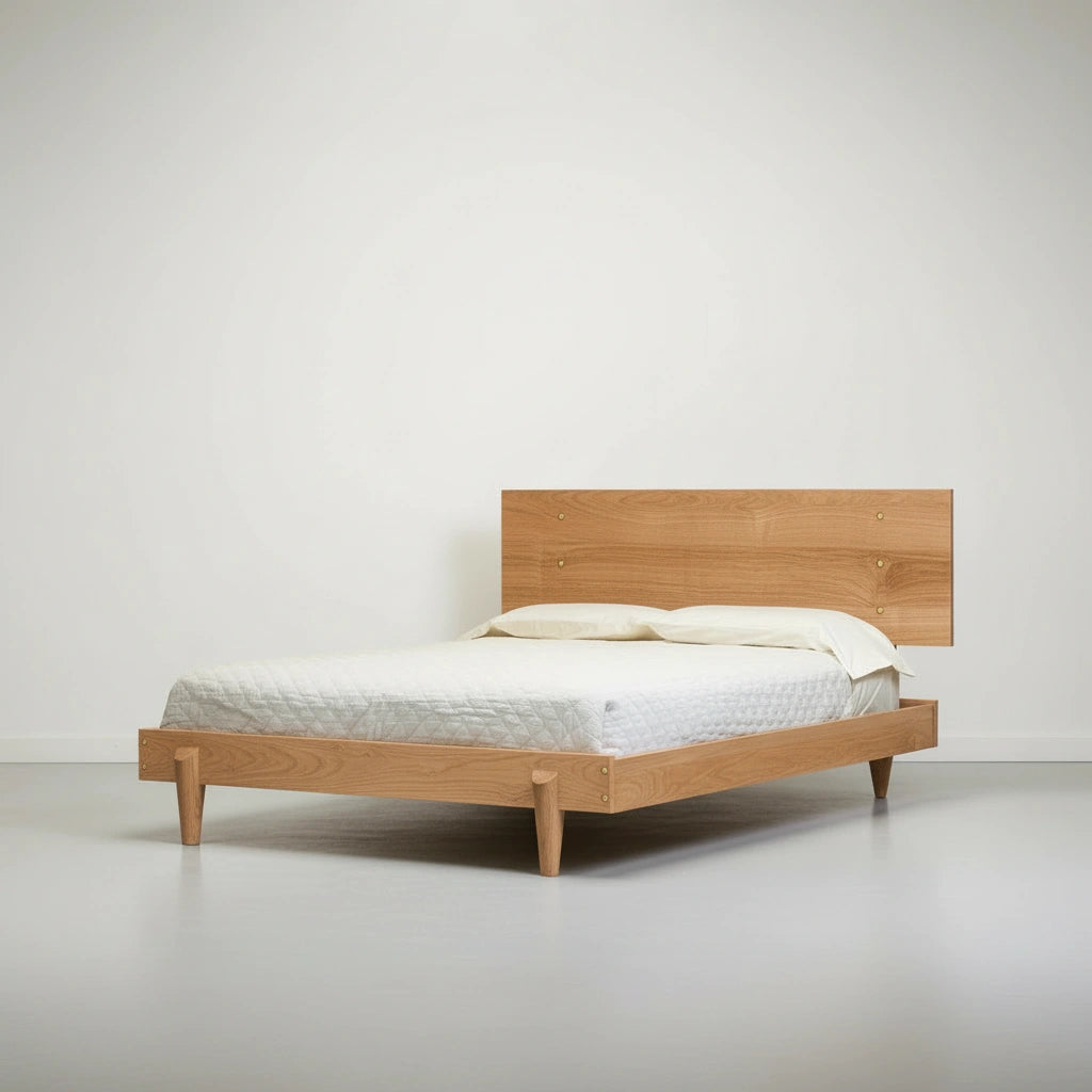 The TY Fine Furniture Apollo Platform Bed, a solid wood modern bed frame in white oak, features a minimalist rectangular headboard and is styled with a white mattress and two pillows in a simple room with white walls and a light floor.
