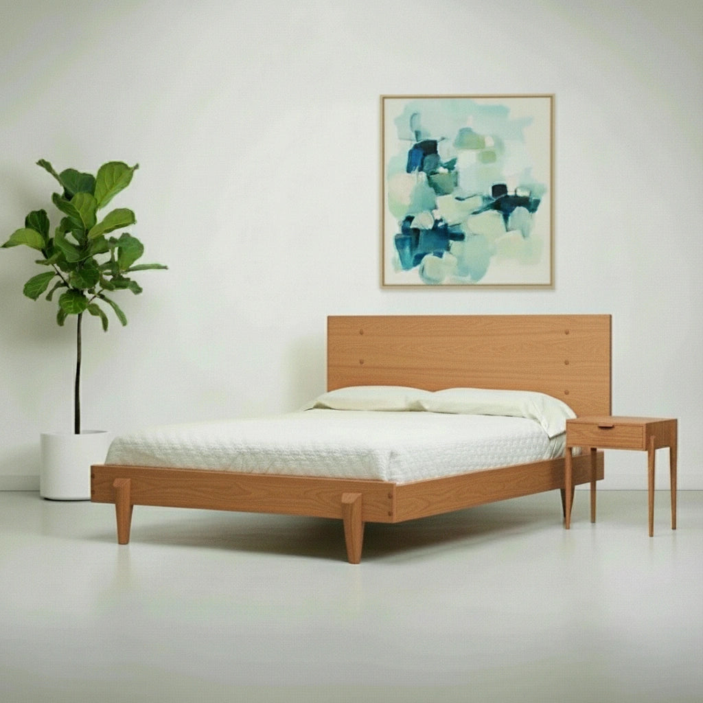 A minimalist bedroom with the TY Fine Furniture Apollo Platform Bed, a solid wood modern bed frame in cherry, paired with a nightstand, white bedding, a potted plant, and an abstract blue-green painting on a plain white wall.