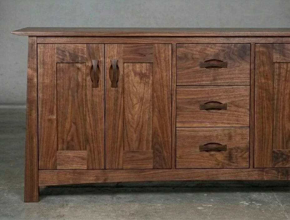 The Enso Credenza & Buffet in Walnut by TY Fine Furniture features solid wood construction, two left cabinet doors, three right drawers with matching handles, and provides stylish dining room storage against a plain gray background.