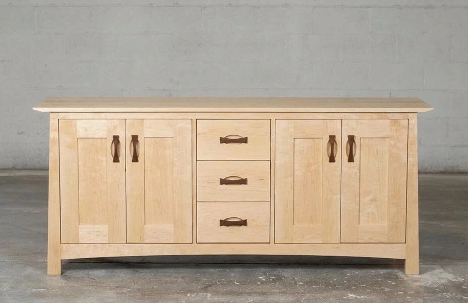 The Enso Credenza & Buffet in Maple by TY Fine Furniture features four central drawers with wooden handles and two side cabinets, providing ample dining room storage, shown here against a plain gray wall.