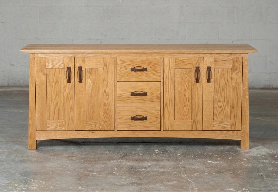 The Enso Solid Wood Credenza Buffet by TY Fine Furniture—handmade from white oak with four cabinet doors, three central drawers, and dark metal handles—offers perfect dining room storage against a simple concrete wall and floor.