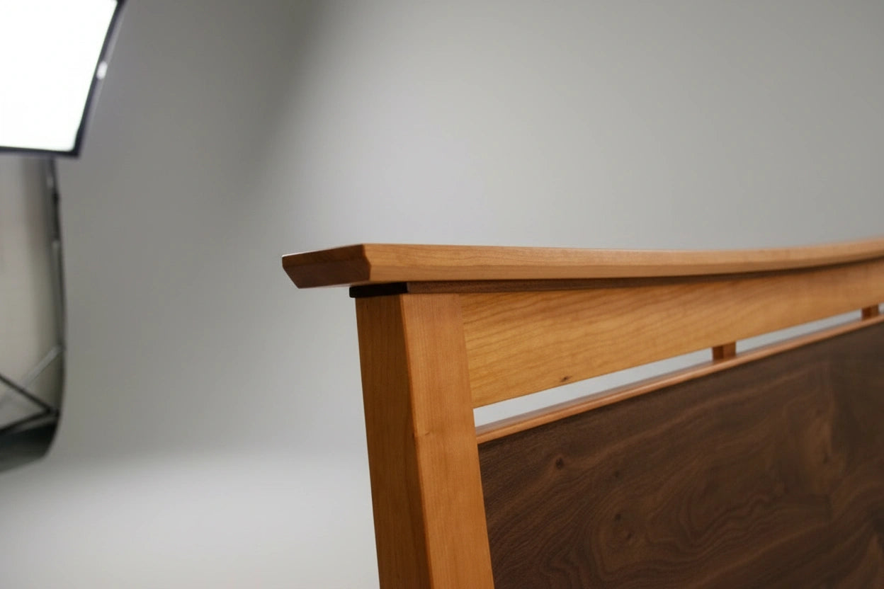 Close-up of the TY Fine Furniture Enso Platform Bed Cherry headboard, featuring a smooth, curved top and natural cherry wood grain, set against a light gray studio background with a softbox light visible on the left.