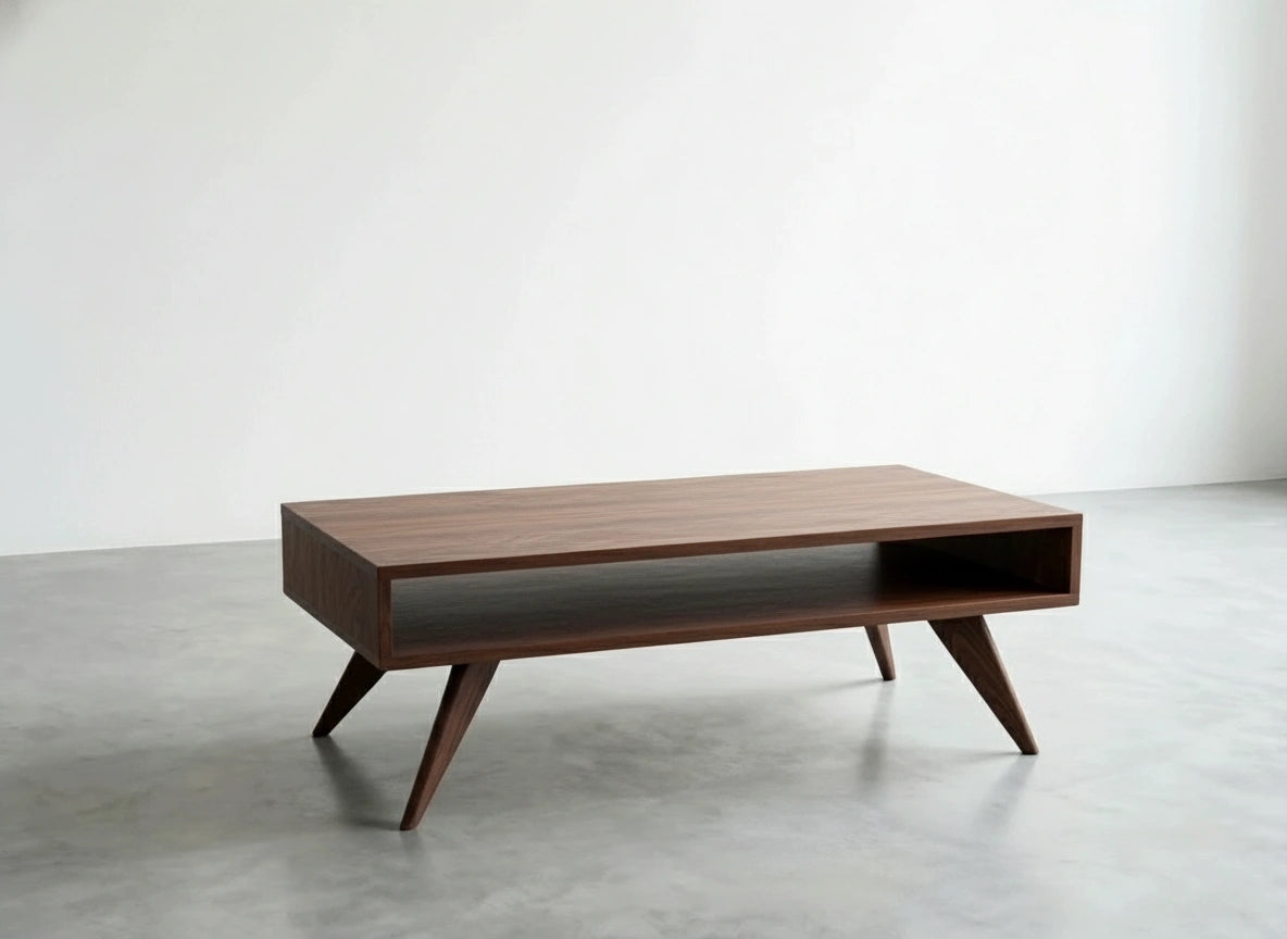 The TY Fine Furniture Modern Coffee Table—Mid-Century Modern, handmade from solid walnut—features four angled legs and an open shelf, shown on a grey floor against a white wall.