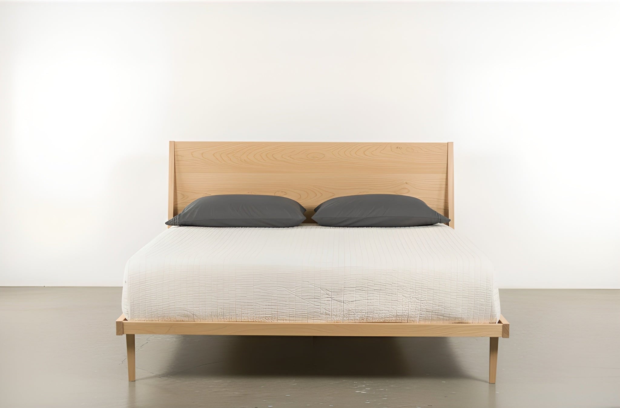 The Modern "ONE" Platform Bed by TY Fine Furniture features a minimalist, handcrafted solid hard maple headboard, dressed in a white textured bedspread with two dark gray pillows, set against a plain white background.