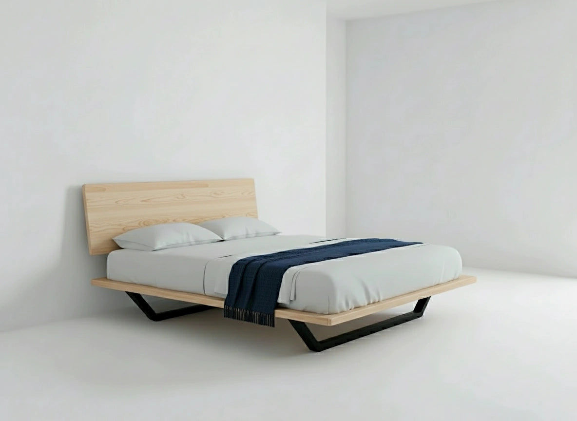 A minimalist bedroom showcases the TY Fine Furniture Nelson Solid Wood Platform Bed Frame in American Hard Maple, dressed in white bedding with two pillows and a dark blue throw, all set against plain white walls and floor.