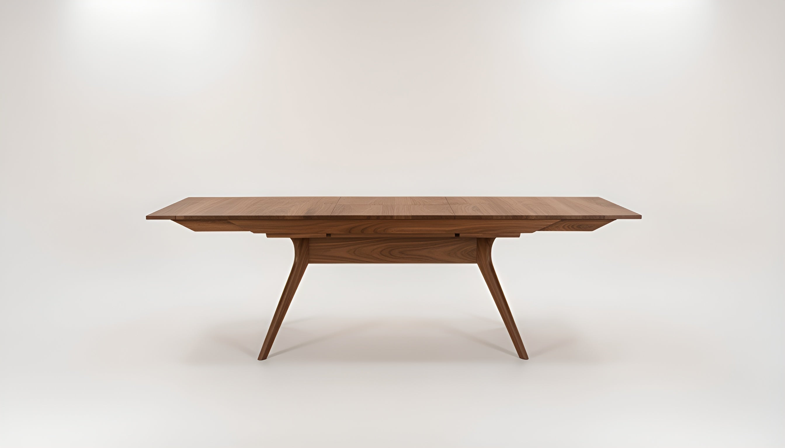 The Strata Extendable Dining Table by TY Fine Furniture features a modern rectangular walnut design with angled legs and a smooth finish, shown against a plain white background.