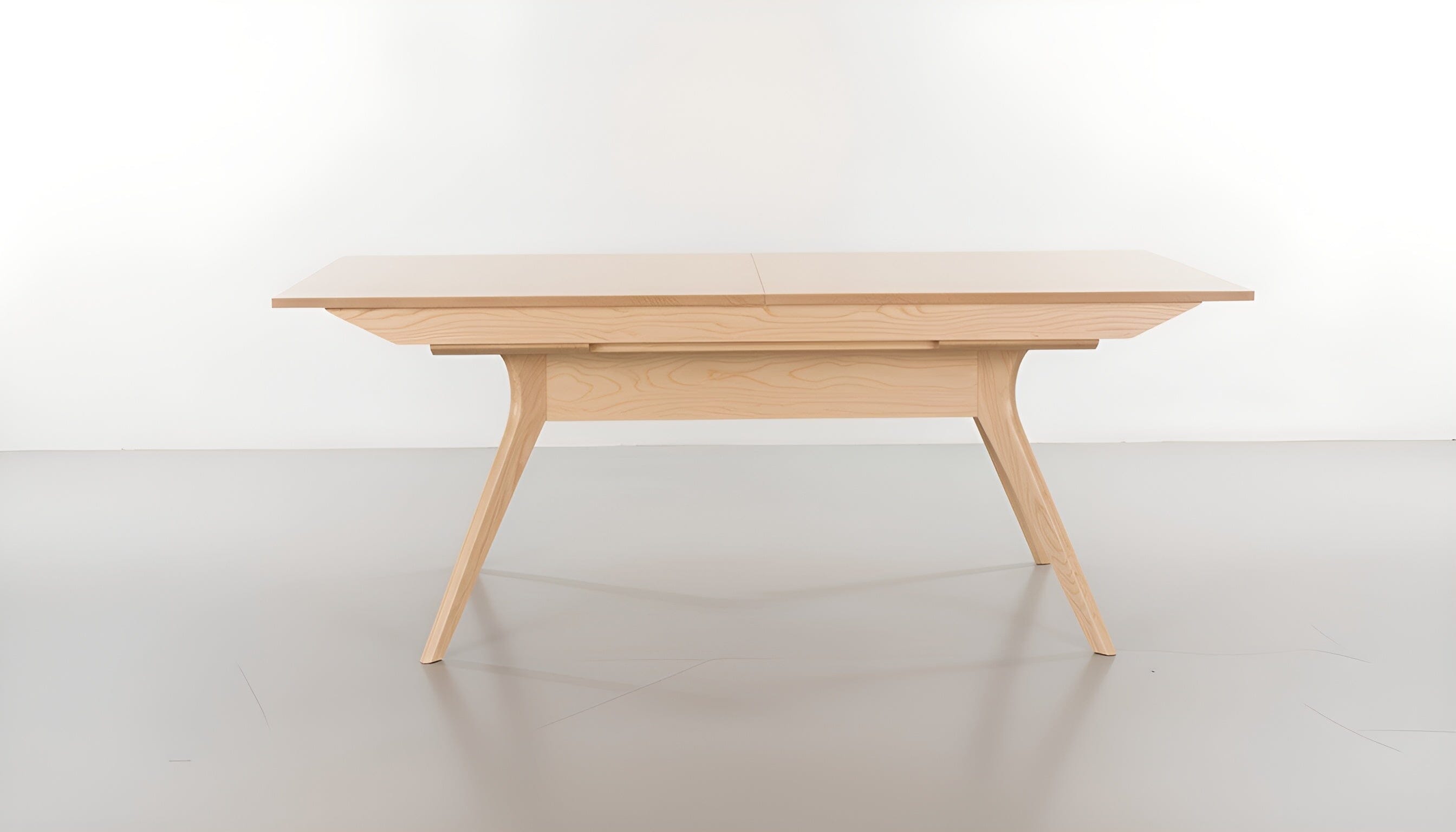 The Strata Extendable Dining Table by TY Fine Furniture features a minimalist design in white oak, with light wood grain, angled legs, and a smooth rectangular top, shown against a plain white background.