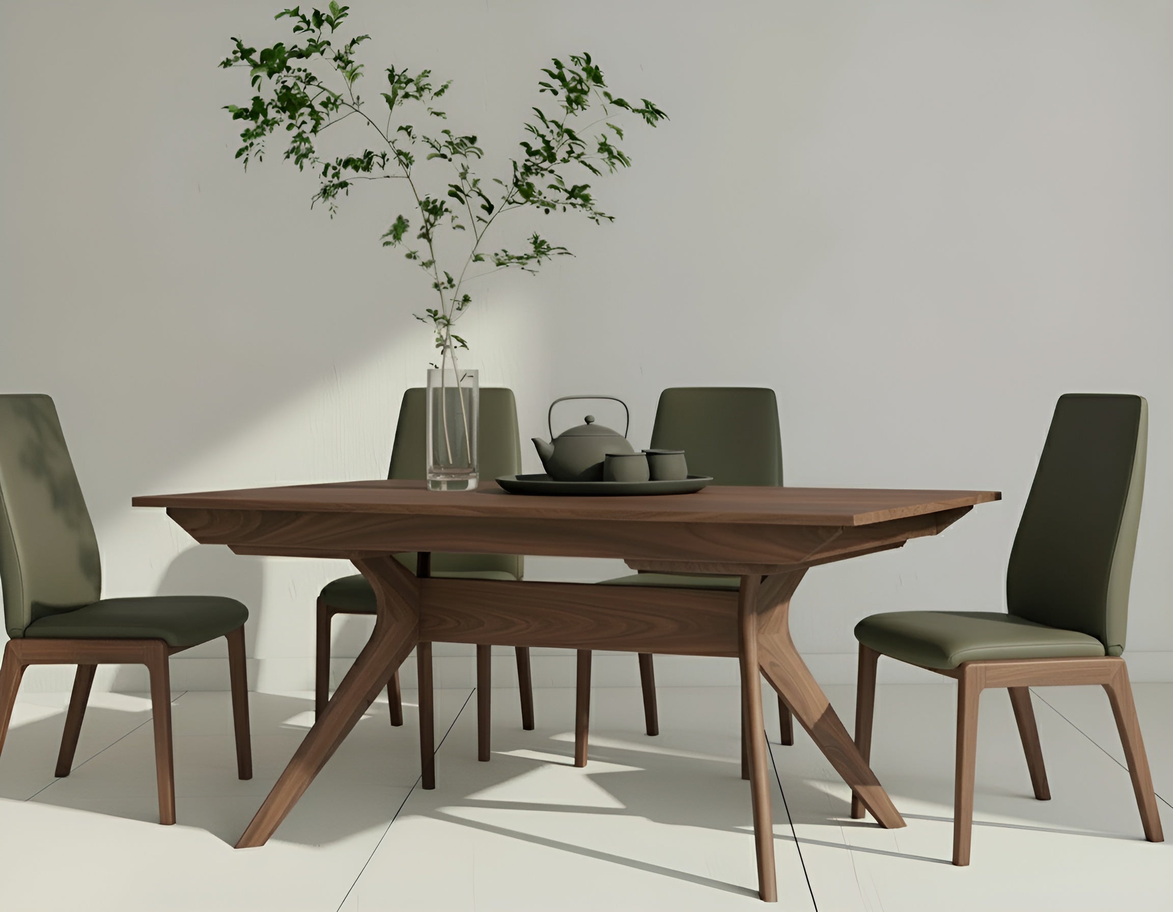 The Strata Extendable Dining Table in walnut by TY Fine Furniture is paired with four olive green chairs, topped with a glass vase of leafy branches and black bowls, set in a bright, minimalist space with white walls and flooring.
