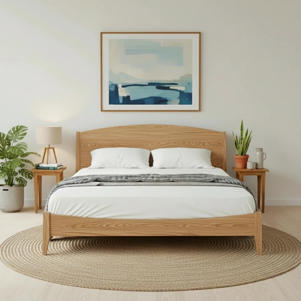 A modern bedroom with a T.Y. Fine Furniture Shaker Platform Bed in white oak, crisp white bedding, two bedside tables with lamps and plants, a large abstract painting above, and a round woven rug on light wood flooring.