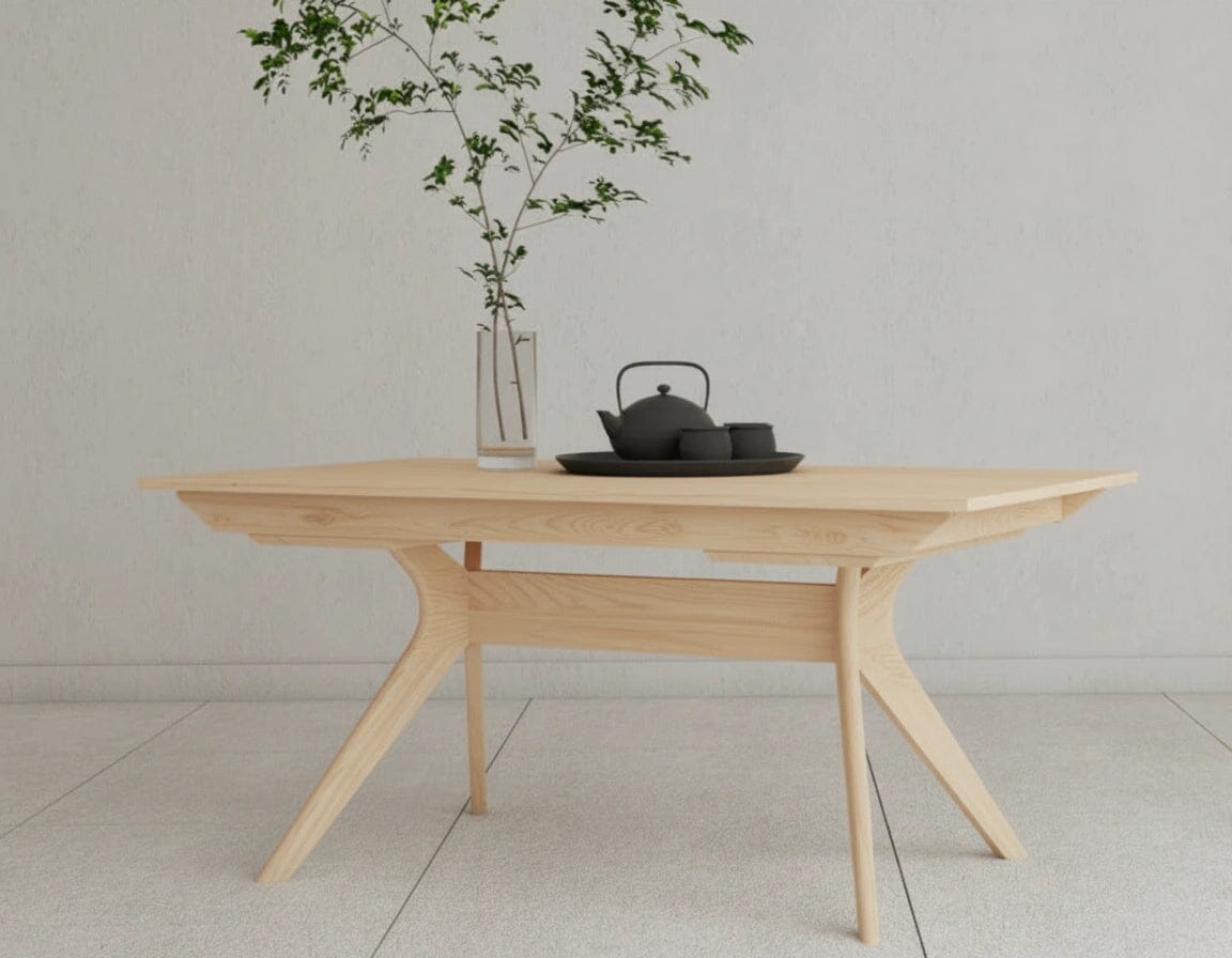 The Strata Extendable Dining Table by TY Fine Furniture, crafted in maple with angled legs, displays a black tea set on a tray and a glass vase with leafy branches, set against a light wall and tiled floor.