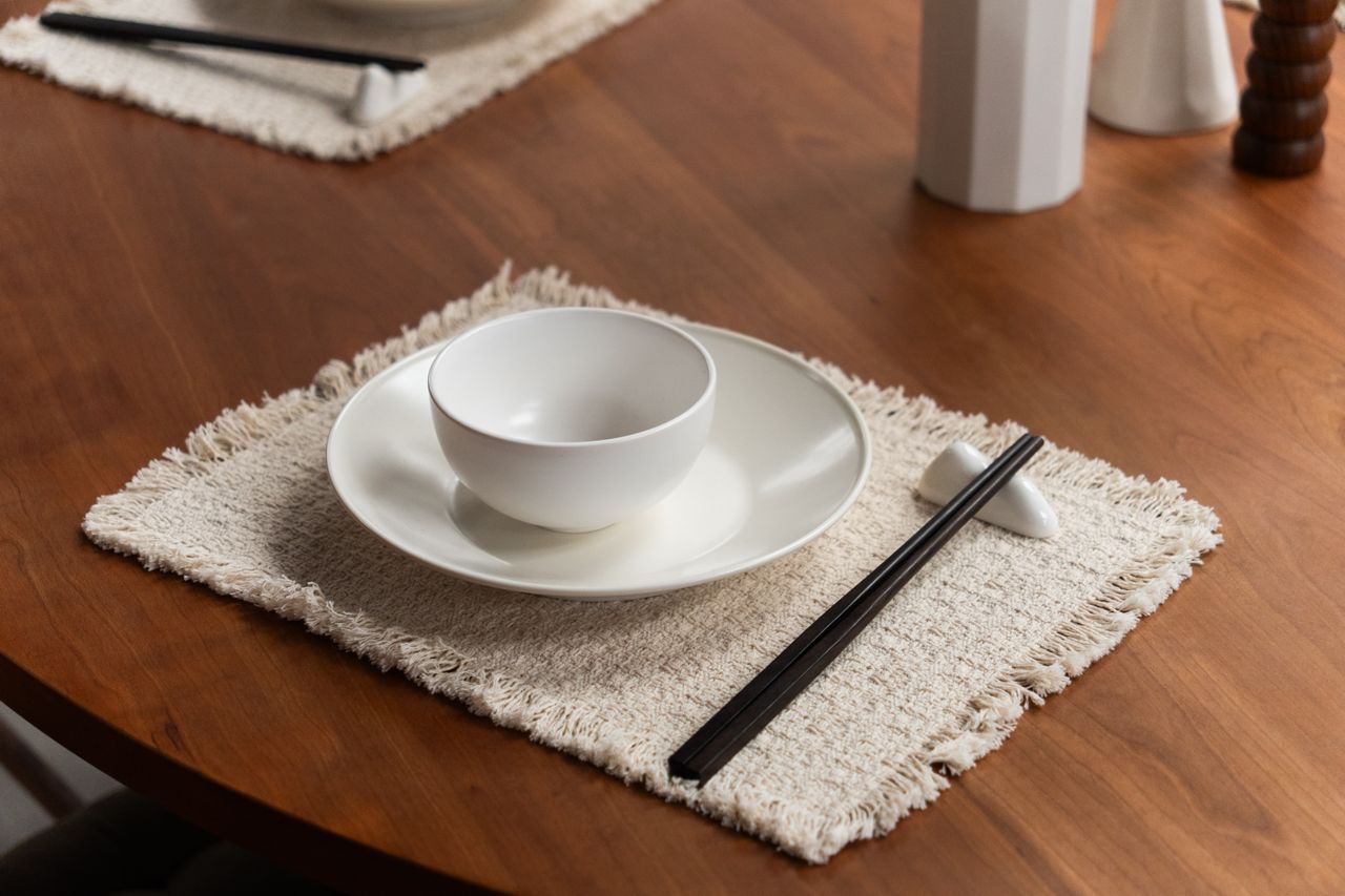 A minimalist dining setup featuring white ceramic crockery and black chopsticks on a wooden table.