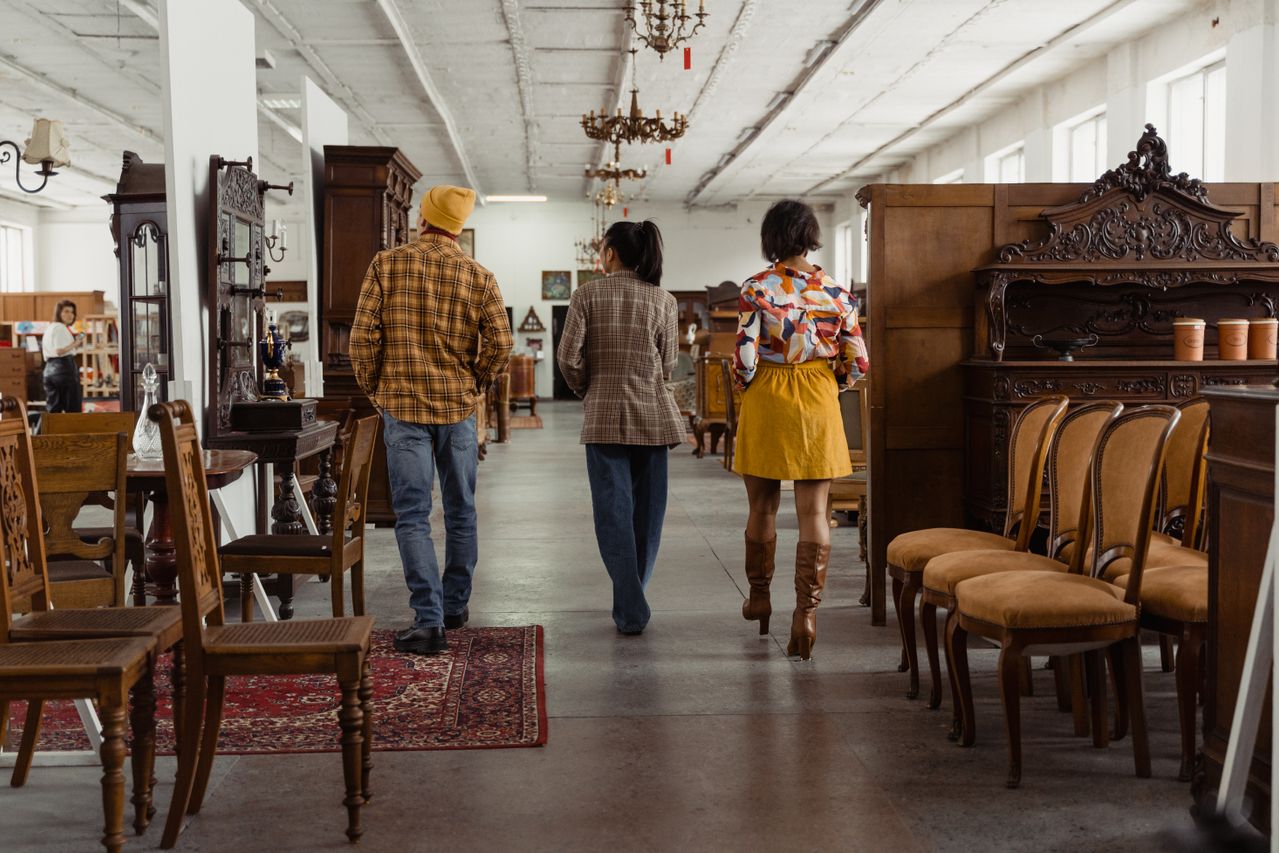 People walking through an antique furniture store, surrounded by vintage chairs and decor