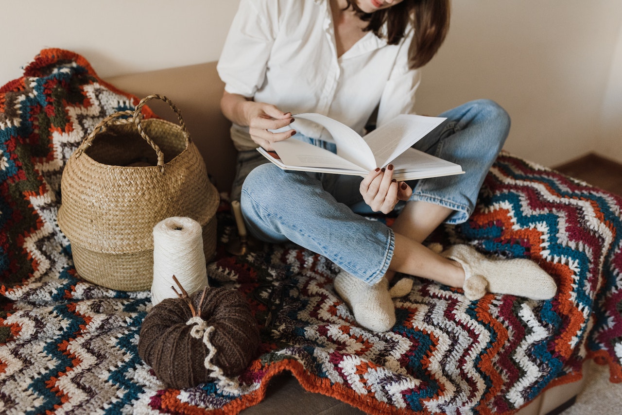 Woman in White Long Sleeve Shirt and Blue Denim Jeans Sitting on Brown and White Textile