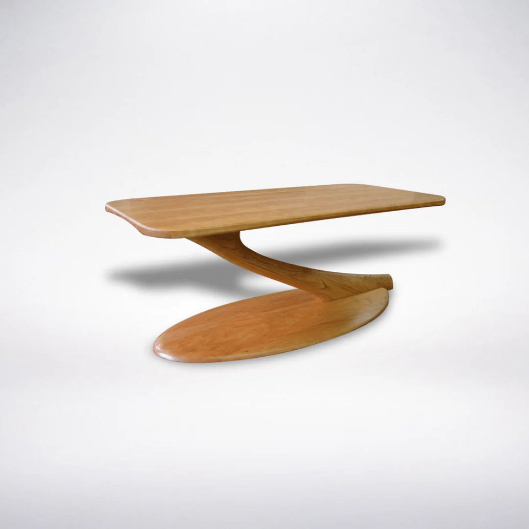 The Cantilever Coffee Table Solid Wood- Cherry by TY Fine Furniture features a sleek, curved base and an elongated oval top. Crafted in the USA for lasting quality, this modern piece stands out against a plain white background.