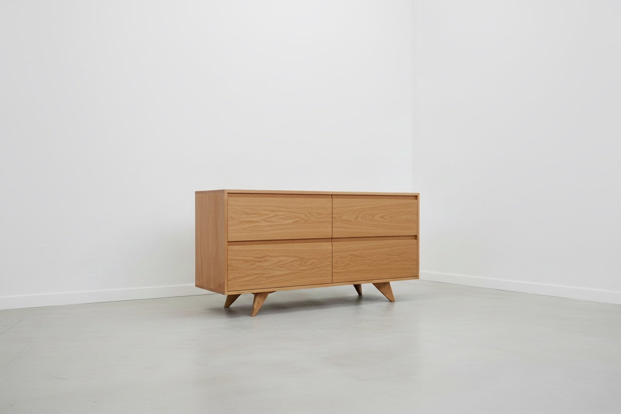 The TY Fine Furniture Modern Mid-Century Dresser in White Oak—crafted from solid wood with four drawers and angled legs—stands in a minimal, white-walled room with a light gray floor.