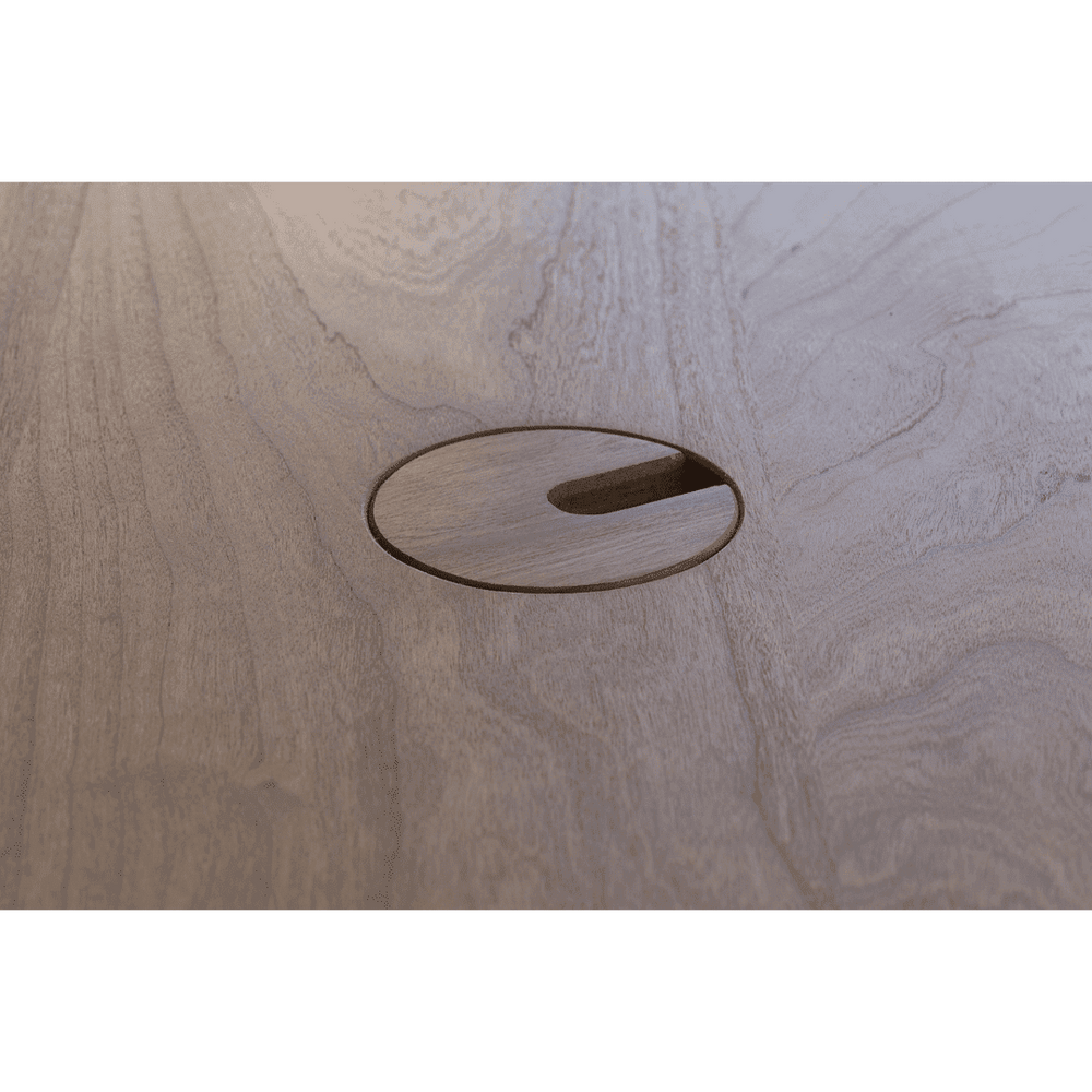 A close-up of a brown wooden desk with a cable management hole