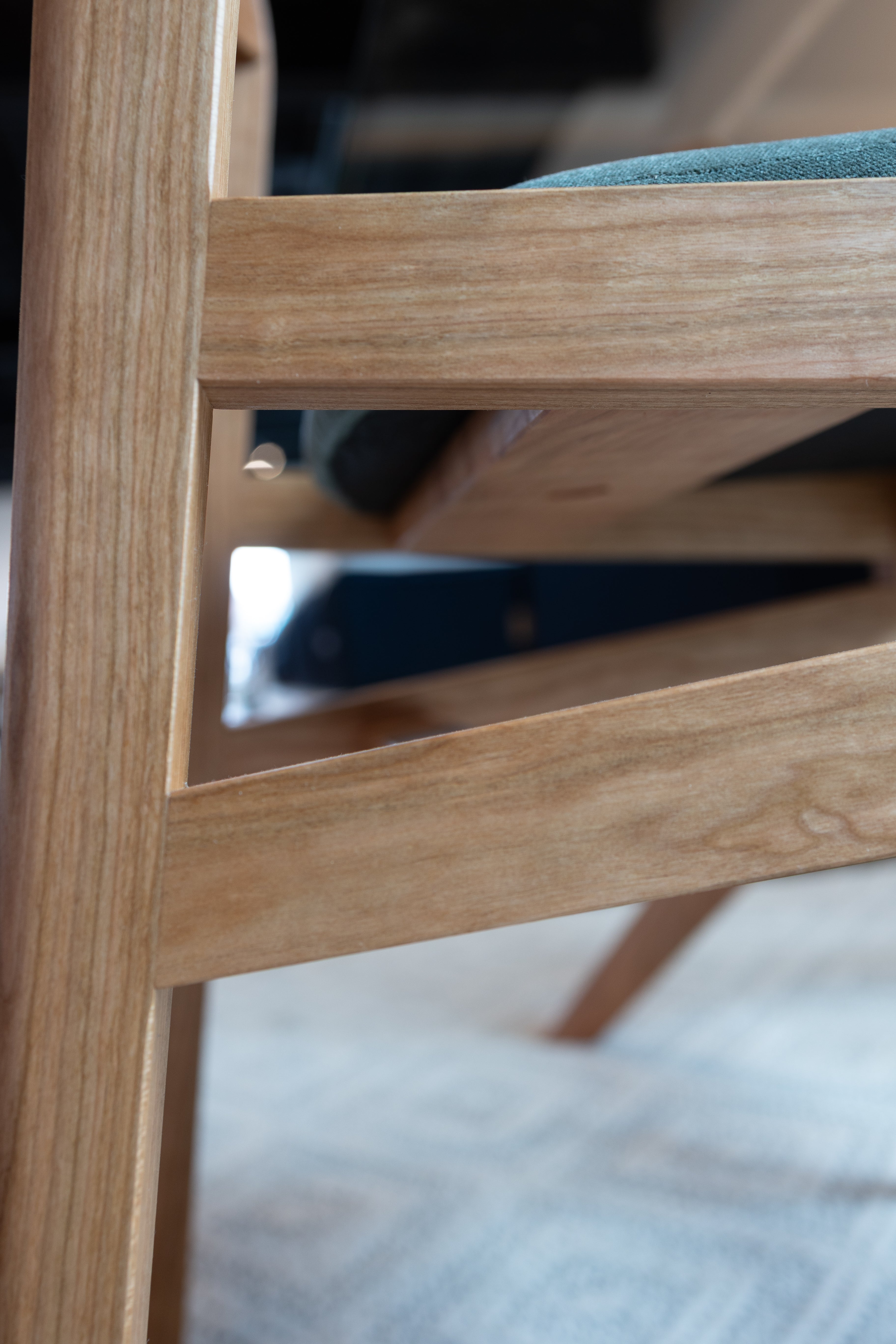 Close-up of the Strata Collection Solid Cherry Dining Chair by T.Y. Fine Furniture, highlighting its light-toned solid cherry wood with an organic finish, a green upholstered seat, and a patterned rug beneath.