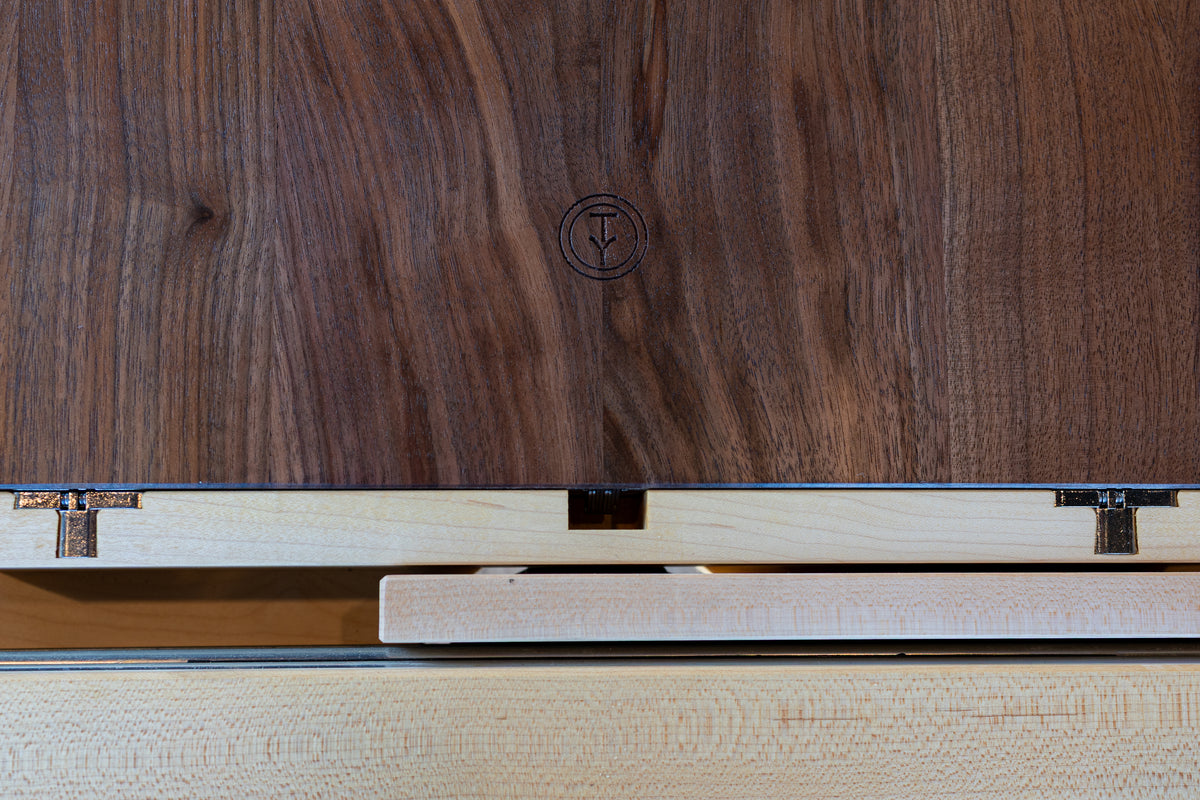 Here’s a rewritten version of your sentence using the provided product data: A close-up of a wooden box with a visible hinge and lid, featuring a circular logo or stamp on the deep cherry surface. The meticulous craftsmanship and attention to detail reflect the quality of the Solid Cherry Extendable Round Dining Table from TY Fine Furniture’s Strata Collection, while the interior showcases lighter wood and expertly executed joinery.