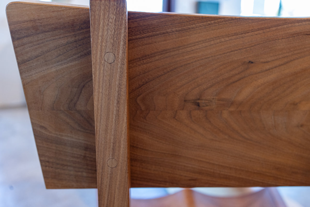 A close-up view of the back of a Solid Cherry Dining Chair from the Enso Collection by TY Fine Furniture, highlighting the rich, warm grain patterns of polished cherry wood and two circular wooden dowels securing the vertical support to the horizontal backrest—a subtle nod to Japanese woodworking traditions that blend seamlessly with contemporary design.