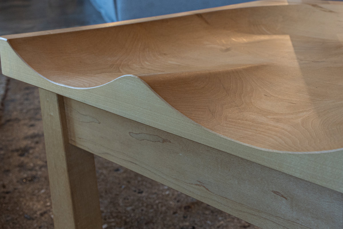 A Solid Cherry Dining Chair from the Enso Collection by TY Fine Furniture—featuring elegantly curved edges and smooth, sculpted lines inspired by Japanese woodworking—stands gracefully on a polished concrete floor, embodying contemporary design.