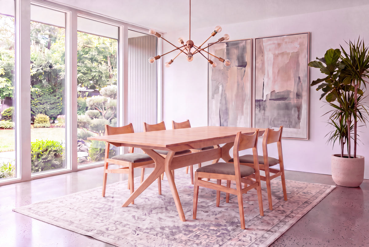 A modern dining room featuring the Solid White Oak Extendable Dining Table from the Strata Collection by TY Fine Furniture, paired with six chairs, large windows overlooking a garden, abstract art on the wall, a geometric chandelier, and a potted plant in the corner.