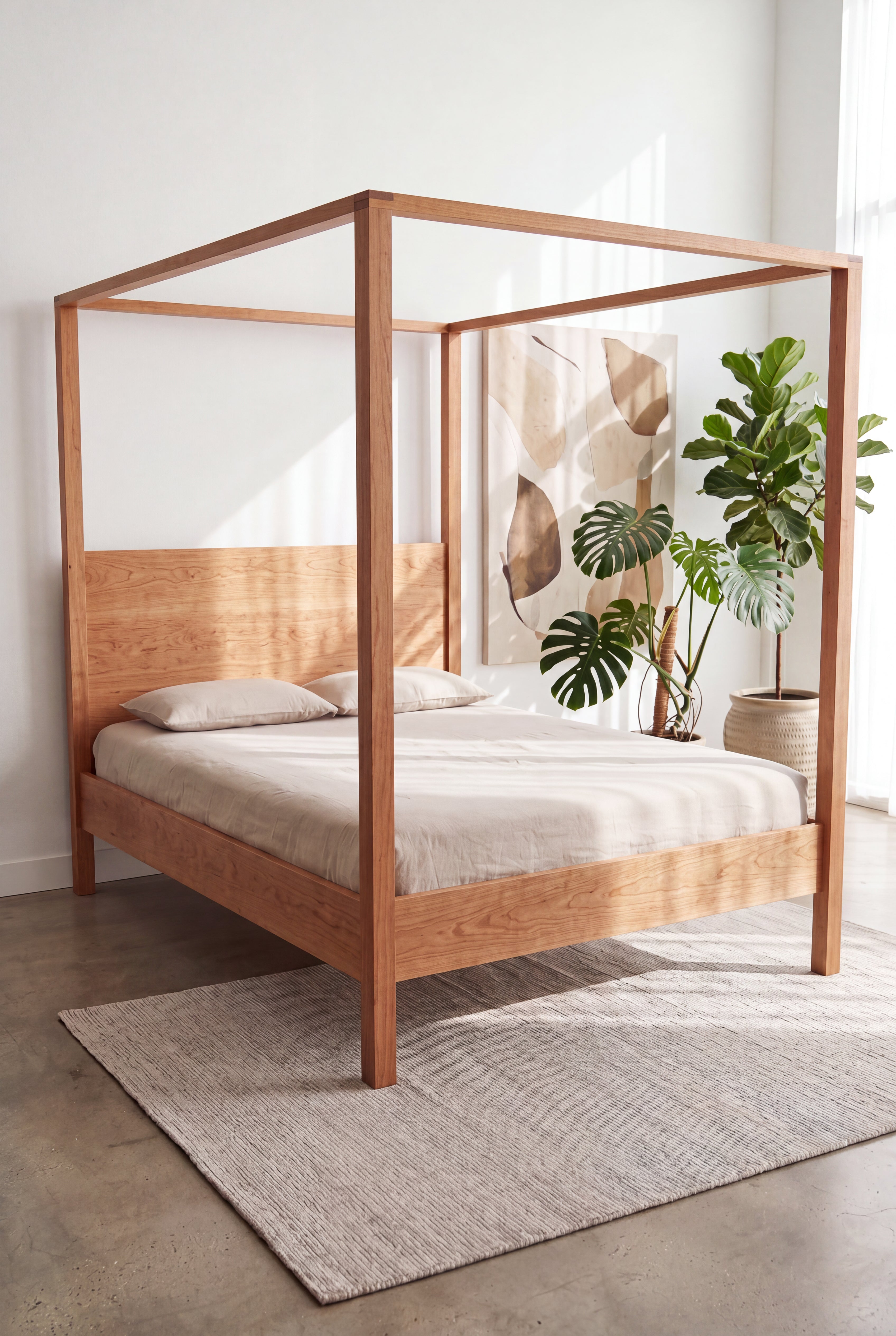 The Modern Four Poster Bed - Solid Wood-Cherry by TY Fine Furniture, dressed in beige bedding, rests atop a textured rug in a minimalist room featuring contemporary furniture. The space is accented with a large green plant and abstract wall art, all beautifully illuminated by natural sunlight.